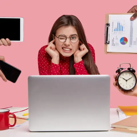 Overwhelmed person at cluttered desk, trapped by endless to-do list, illustrating the Busyness Trap. Maximise time.