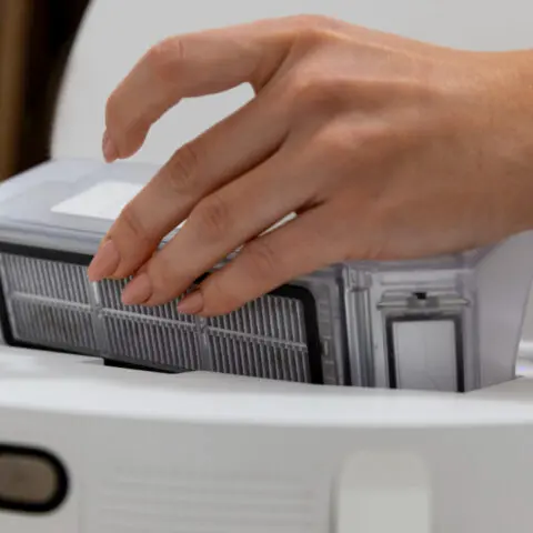 Close-up of hands performing Copier maintenance tips, cleaning paper dust to maximise machine longevity. Short, descriptive, purposeful.
