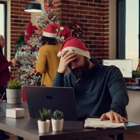 Stressed employee hiding behind a plant at a Christmas party, highlighting Office Party Anxiety Survival Guide.