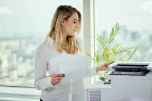 A stack of paper invoices being fed into an office photocopier's automatic document feeder using basic invoice scanning tools.