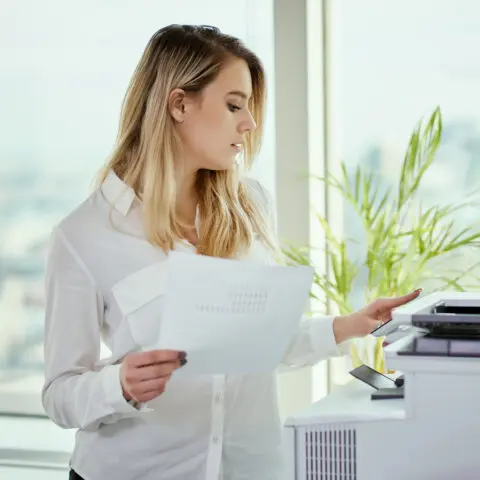 A stack of paper invoices being fed into an office photocopier's automatic document feeder using basic invoice scanning tools.