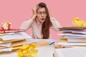 Stressed office worker at a desk overwhelmed by towering piles of paperwork and documents.