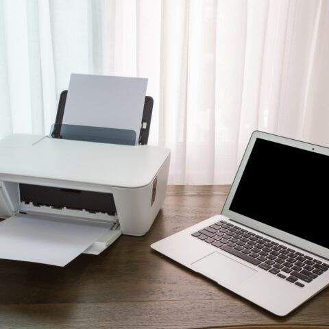 Cluttered desk with cheap, broken personal inkjet printer and expensive ink, contrasting with a smooth MFD, illustrating Personal Printer Desk Demons.