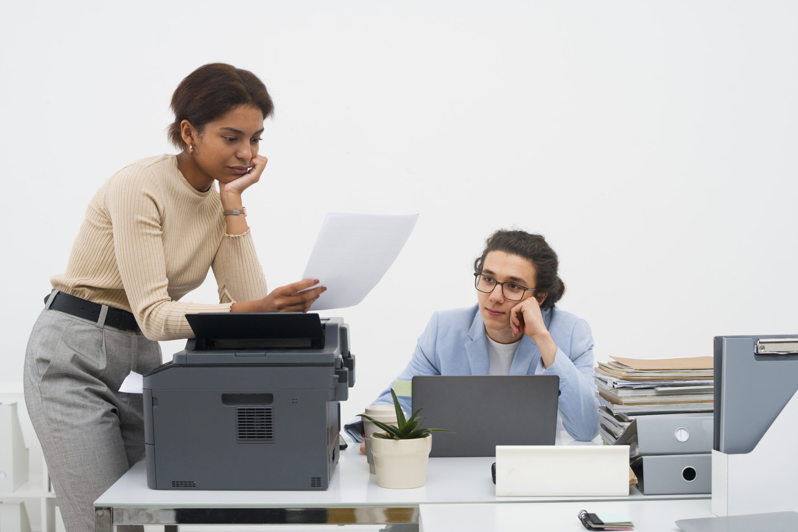 An exasperated employee is bent over a photocopier, trying to clear a paper jam