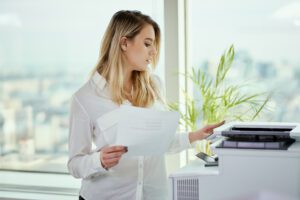 A stack of paper invoices being fed into an office photocopier's automatic document feeder using basic invoice scanning tools.