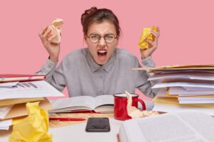 Stressed office worker at a desk overwhelmed by towering piles of paperwork and documents.
