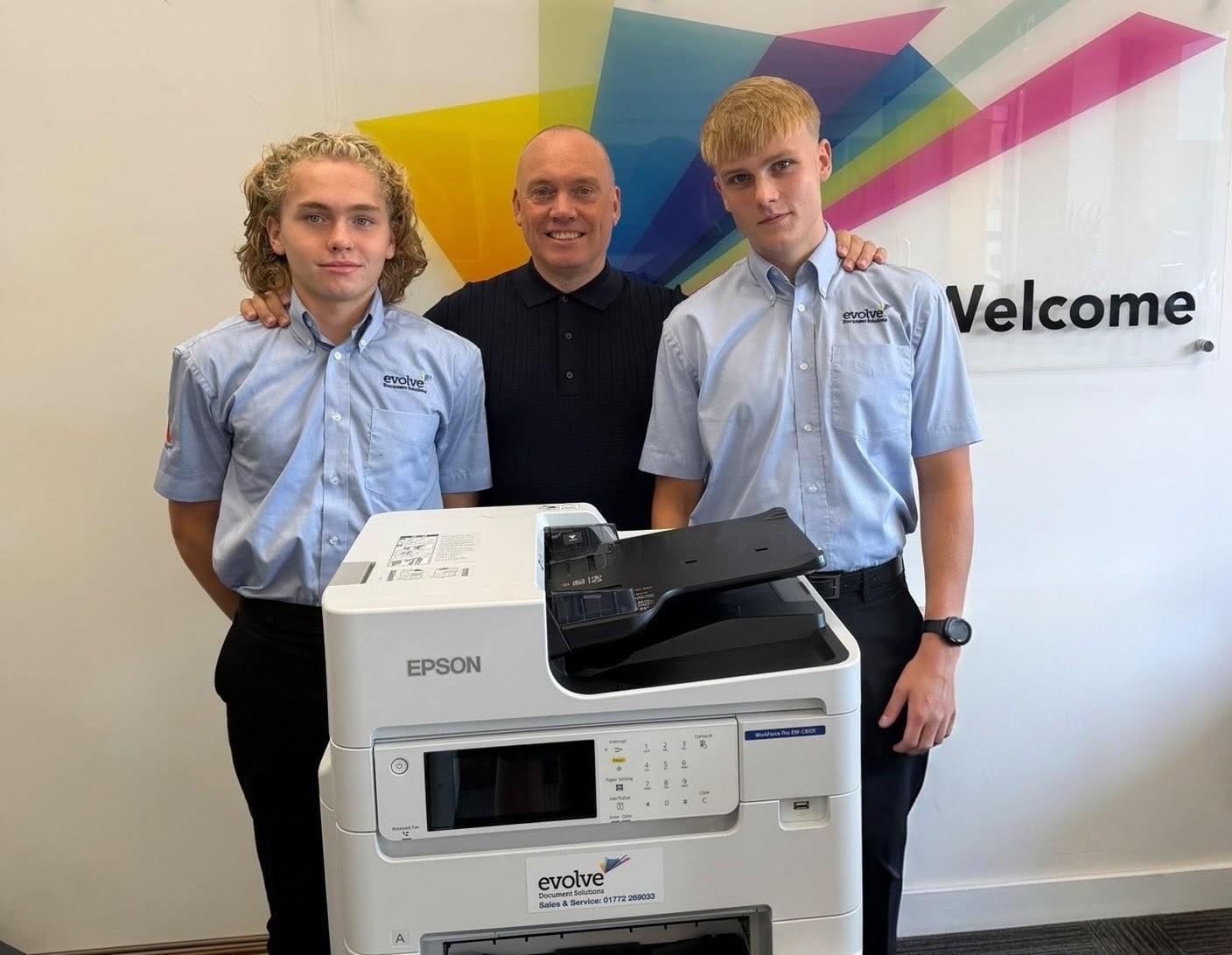 Two young technical apprentices work together inspecting and repairing modern office printer equipment.